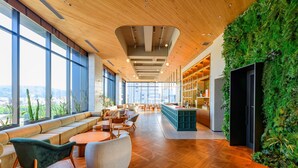 Un amplio y moderno salón con techo de madera, ventanas grandes y una pared verde con plantas.