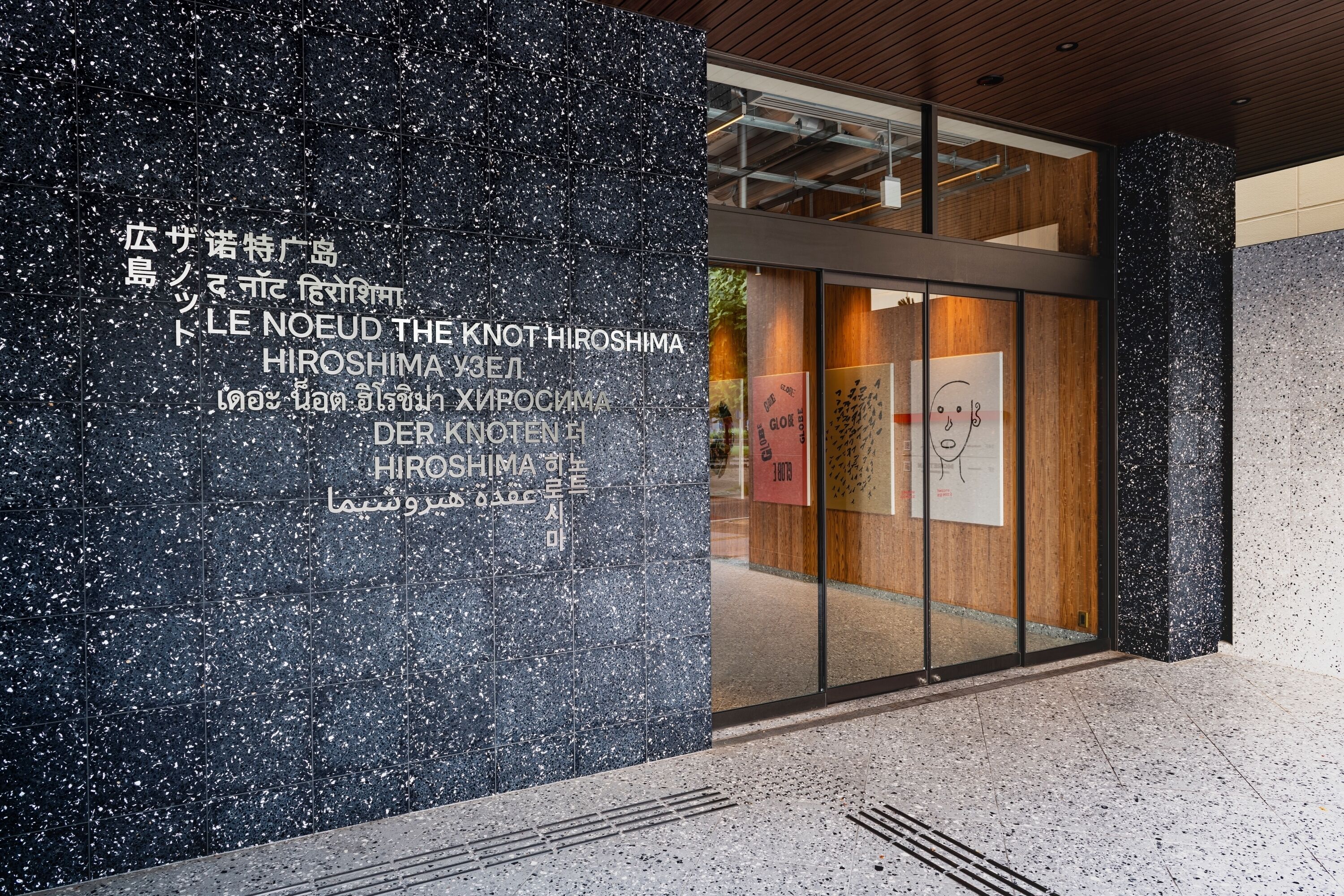 A modern building entrance with a dark speckled facade and glass doors.