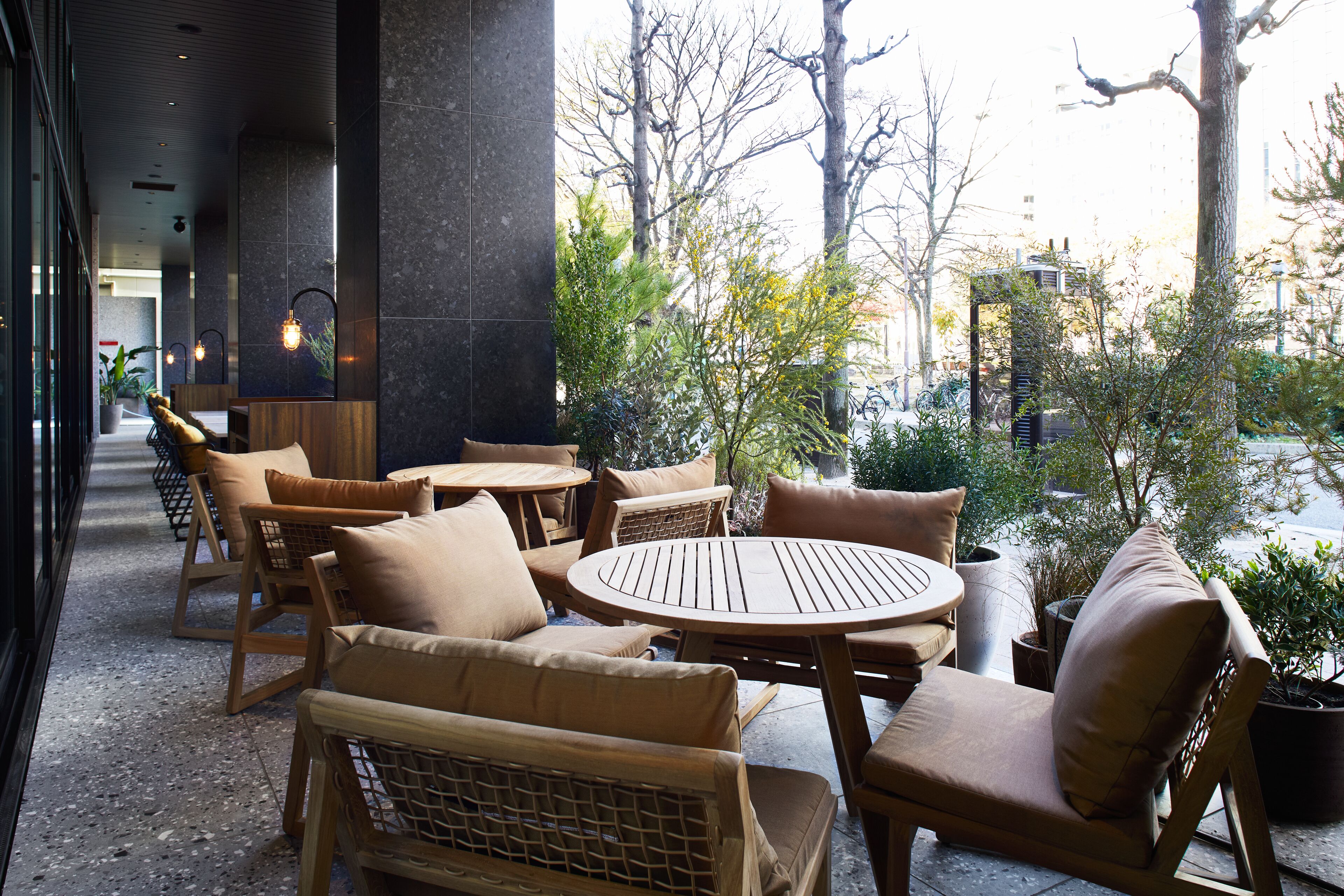 Un espace patio aménagé avec des meubles en osier et une table ronde, entouré de plantes en pot et d’arbres.