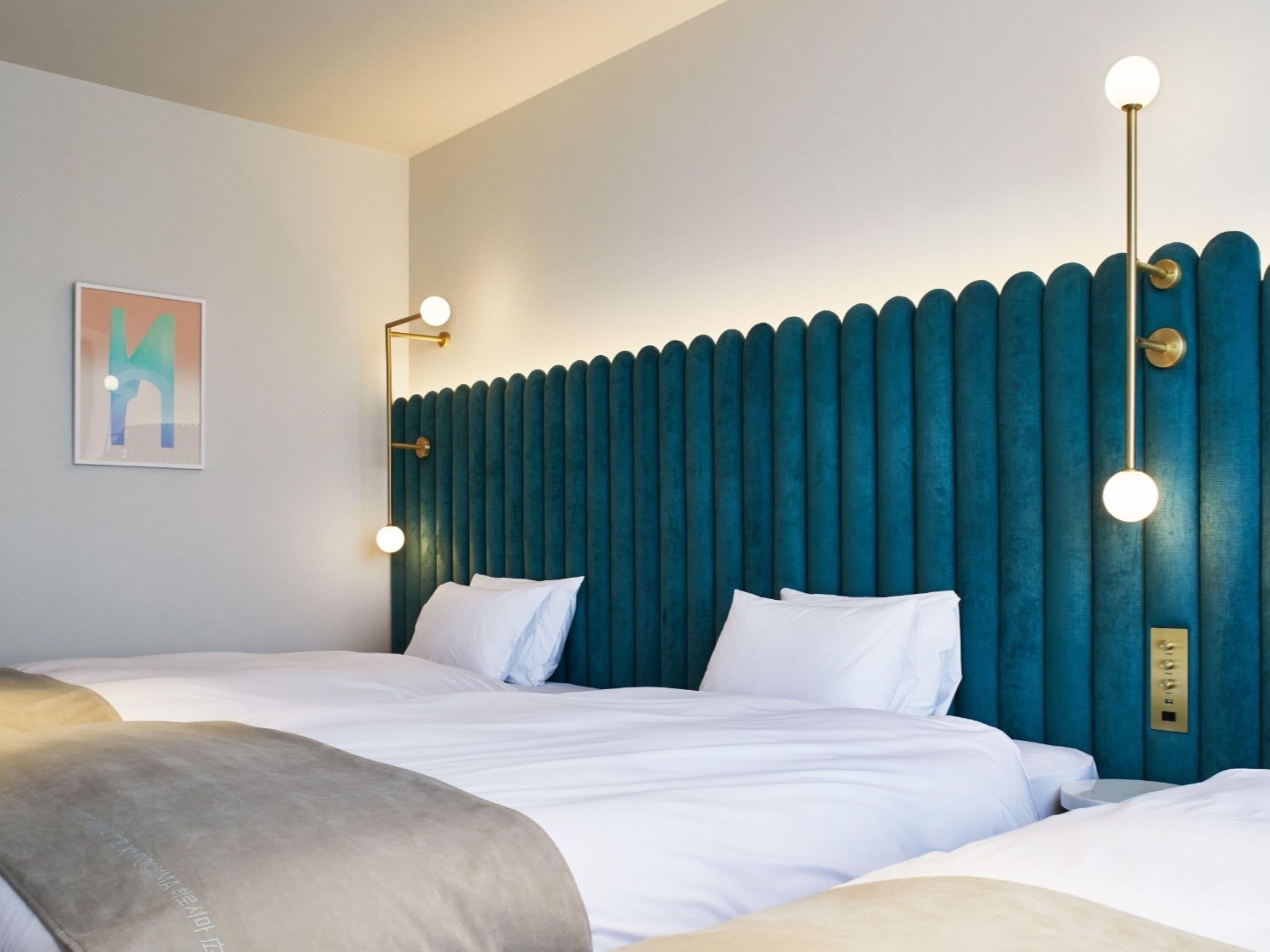 A hotel room with a large bed, two bedside tables, a wall-mounted light fixture, and a framed artwork on the wall.