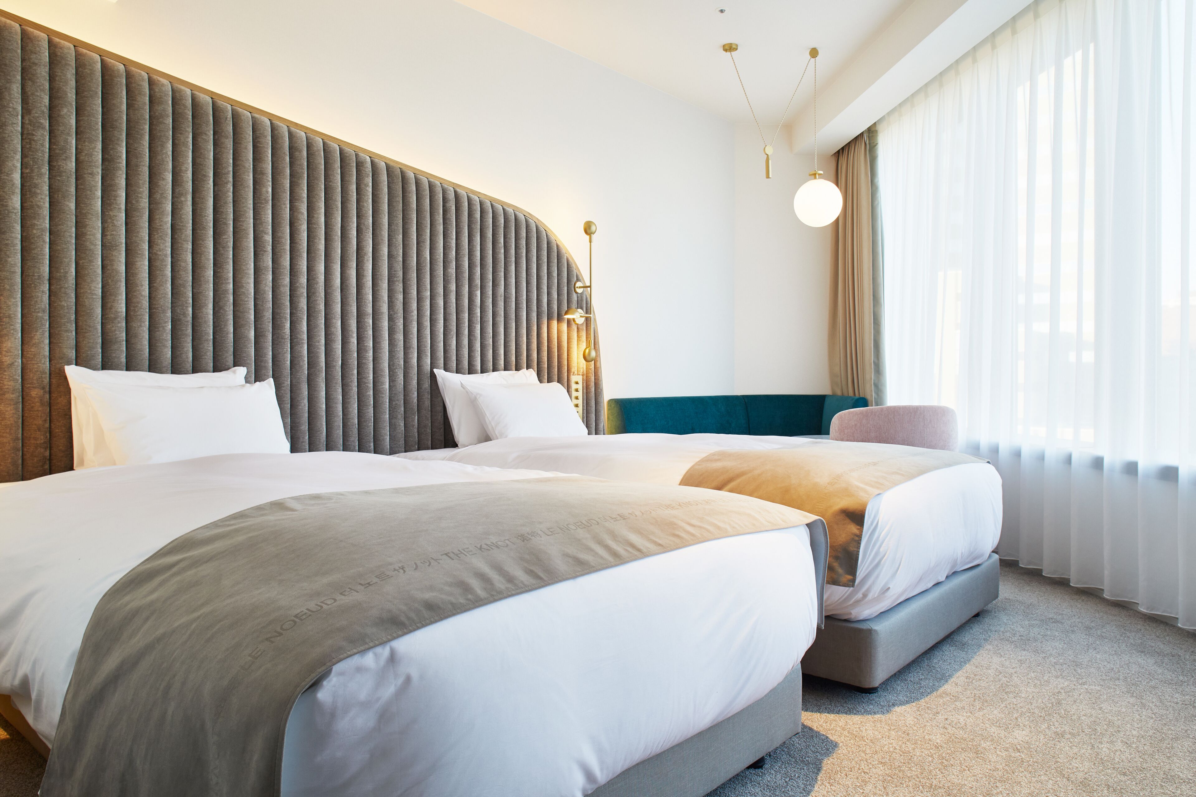 A hotel room with two beds, a large window with sheer curtains, and a modern headboard.