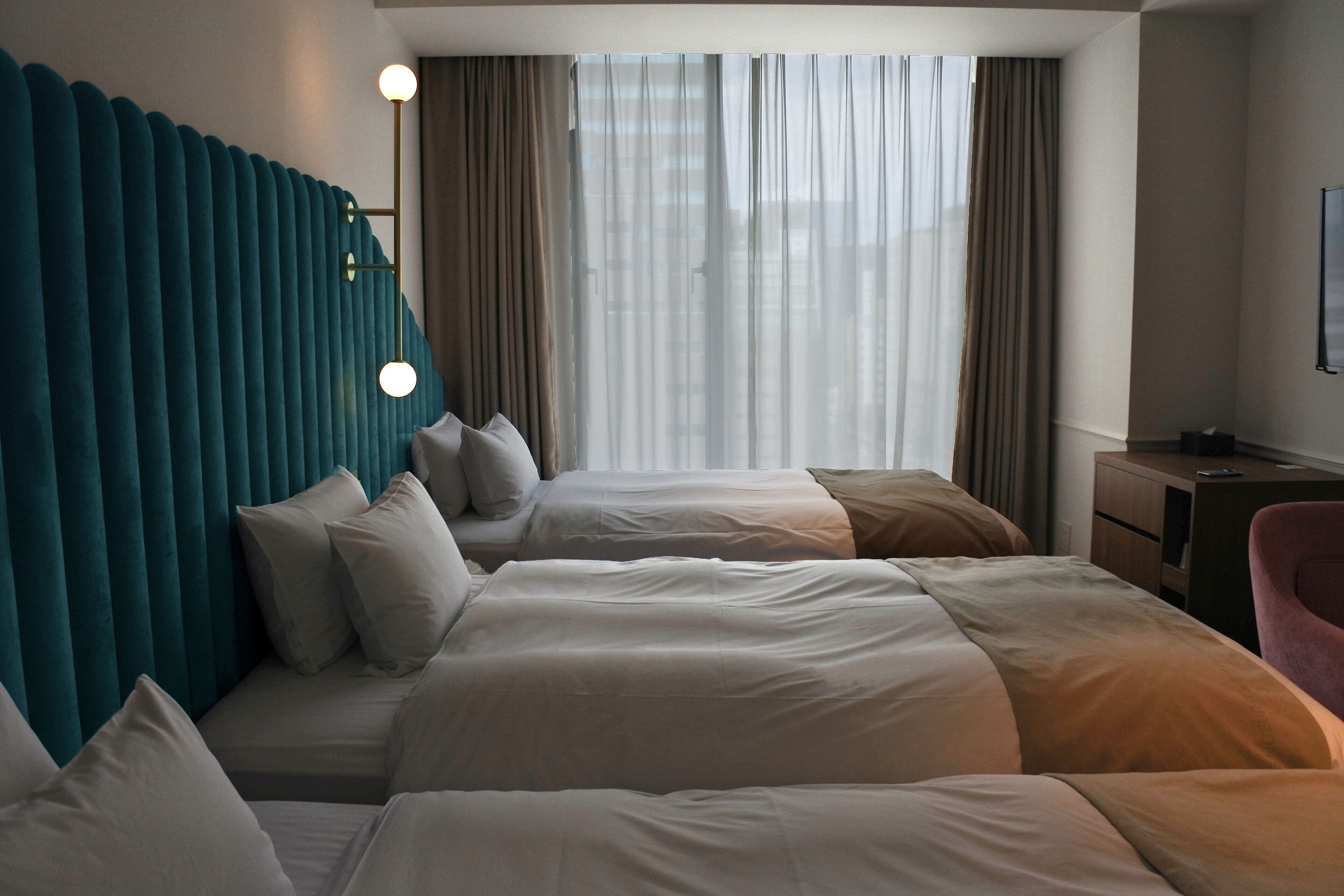 A hotel room with a large bed, a desk, and a chair. There are curtains and a window with blinds.