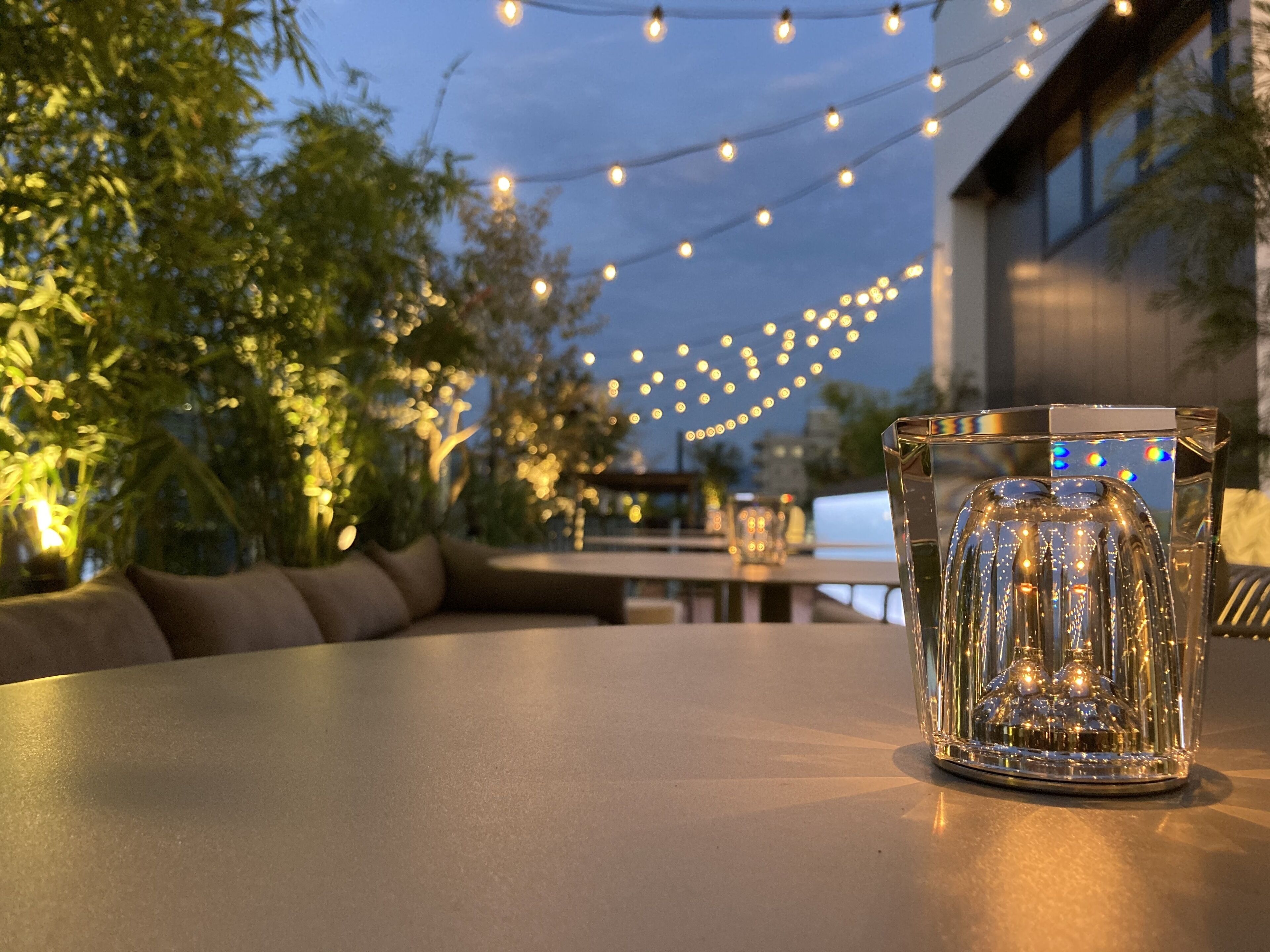 Uma mesa com um castiçal de vidro transparente, luzes de Natal ao fundo e vista para o exterior.