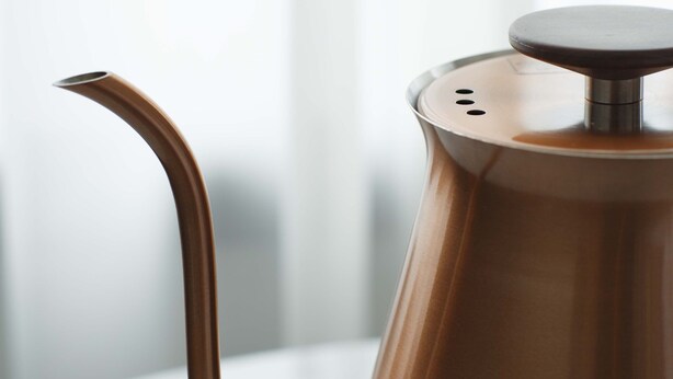 A copper-colored coffee pot with a spout and a lid on a white surface. - THE KNOT Hiroshima (Hiroshima)