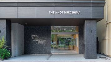 The entrance to The Knot Hiroshima with a modern design, featuring a glass door and a signboard with multiple languages.