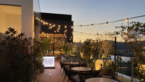 Un patio al aire libre con luces colgantes, plantas en macetas y mesas y sillas redondas.