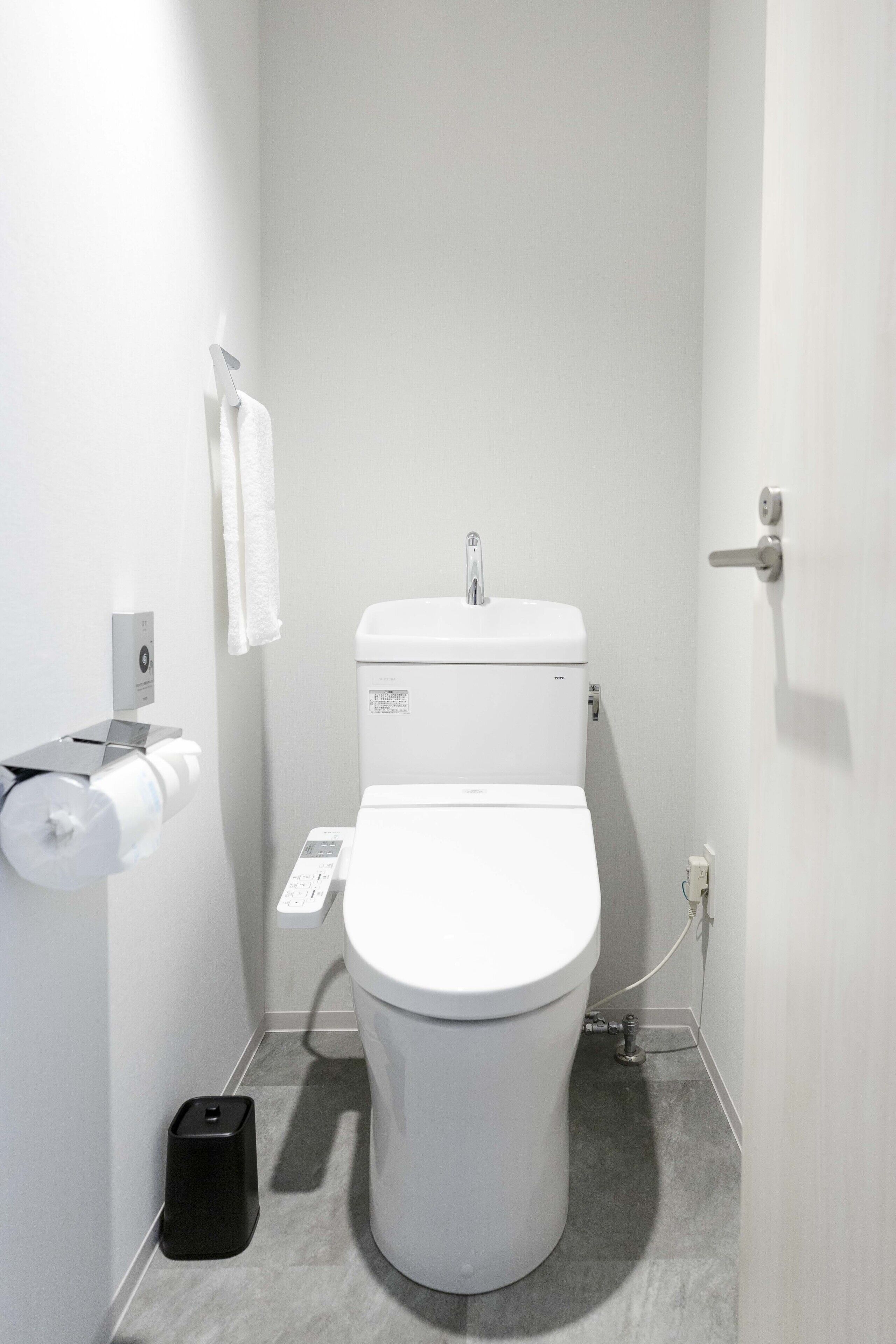 Une salle de bain moderne et compacte, avec des toilettes blanches, un distributeur d’essuie-tout et une poubelle.