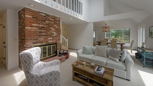 A spacious living room with a brick fireplace, a white sofa, and a dining area with a table and chairs.
