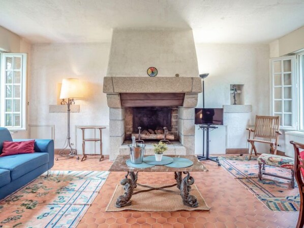 A living room with a stone fireplace, a blue sofa, a television, and a patterned rug.