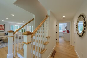 Un interior moderno con una escalera de madera, una zona de cocina y un espacio de sala con sofá y mesa de centro.