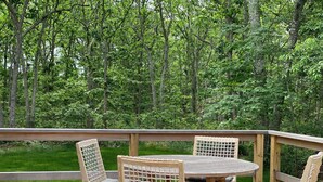 Une terrasse en bois avec une table ronde et quatre chaises, entourée d’une balustrade en bois, donnant sur une forêt dense.