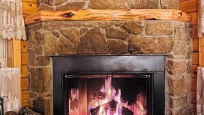 Una chimenea de piedra con fuego encendido, rodeada de paredes de madera y un repisa de madera.