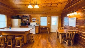 Una cocina estilo cabaña con pisos de madera, una isla central con taburetes, una mesa de comedor y un refrigerador.