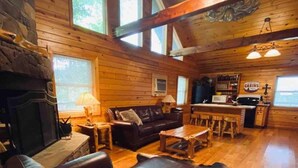Interior acogedor de una cabaña con chimenea, sofá de cuero, mesa de comedor de madera y pared de piedra.