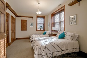 Un dormitorio con dos camas, puertas de madera, una lámpara en el techo y ventanas con persianas.