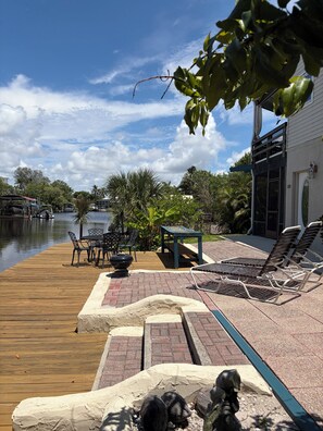 A wooden deck with outdoor furniture, a grill, and a view of a river.