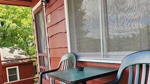 A wooden deck with a table and two chairs, a window with a screen, and a door with the number 2 visible. - The Gold Eagle Cottage 2 (Lake George)