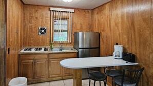 A compact kitchen with wooden walls, a stainless steel refrigerator, a sink, a stove, and a small table with two stools. - The Gold Eagle Cottage 2 (Lake George)