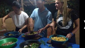 Tres personas preparando comida en una mesa con varios platos y tazones.