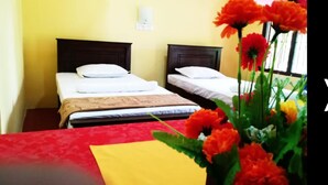 Una habitación de hotel con dos camas, una mesa roja y un jarrón de flores naranjas.