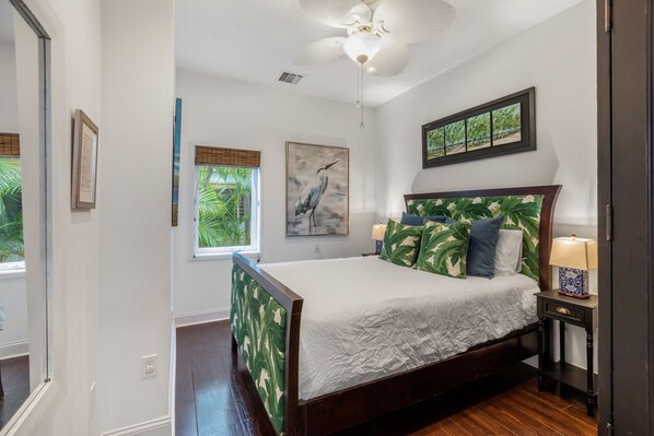 A bedroom with a bed, a nightstand, a ceiling fan, and framed artwork on the walls.
