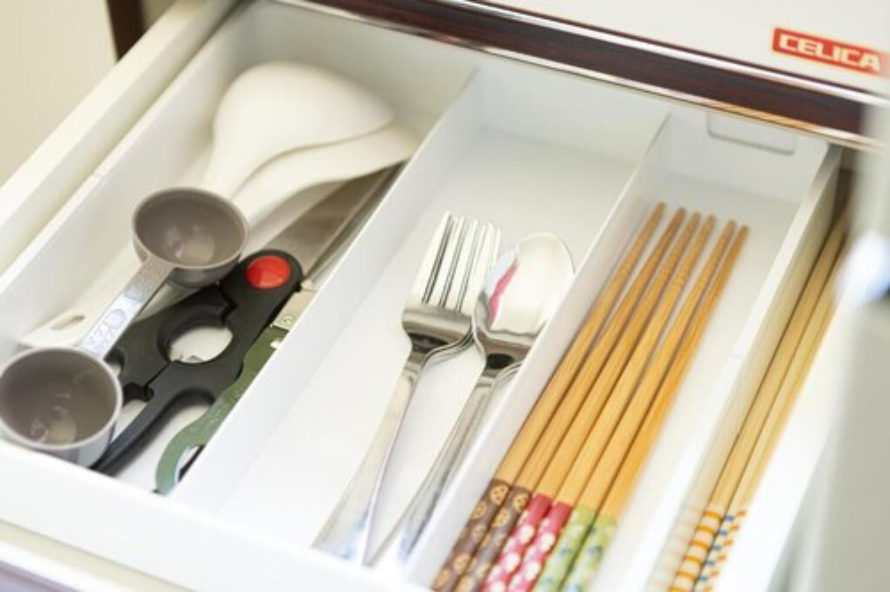 Uma gaveta com vários utensílios, incluindo colher, garfo, faca, pauzinhos e xícaras medidoras.
