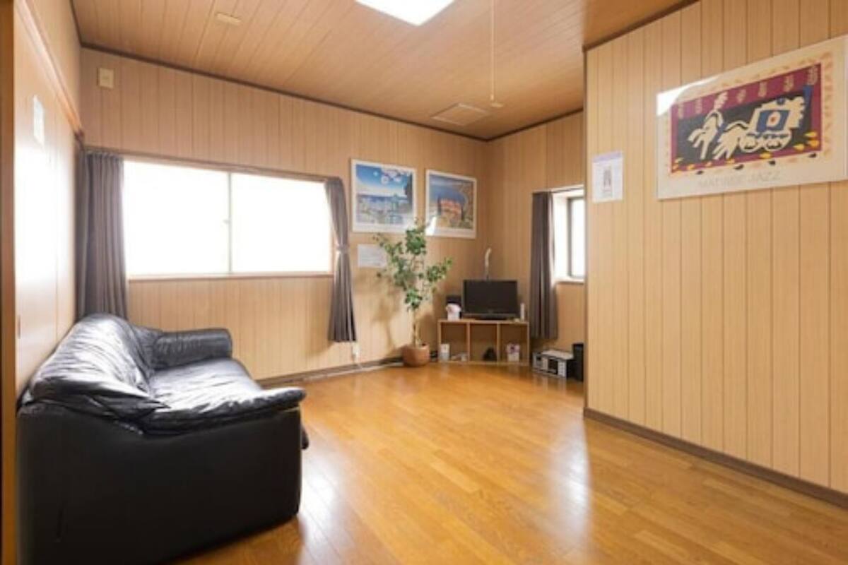 Una sala de estar amplia con sofá de cuero, suelo de madera, televisor y cuadros enmarcados en las paredes.
