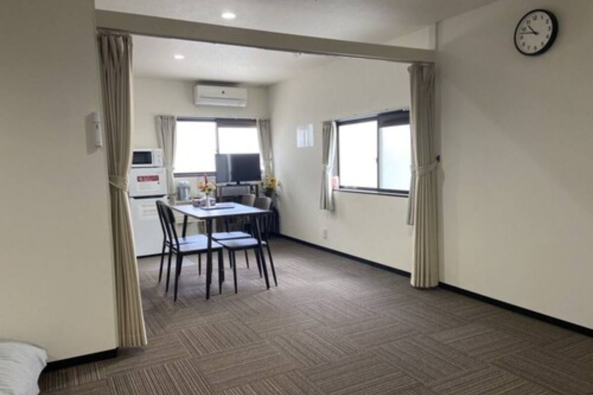Una habitación de hotel con cama, zona de comedor con mesa y sillas, kitchenette y un ventanal grande.