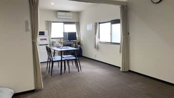 A hotel room with a bed, a dining area with a table and chairs, a kitchenette, and a large window.