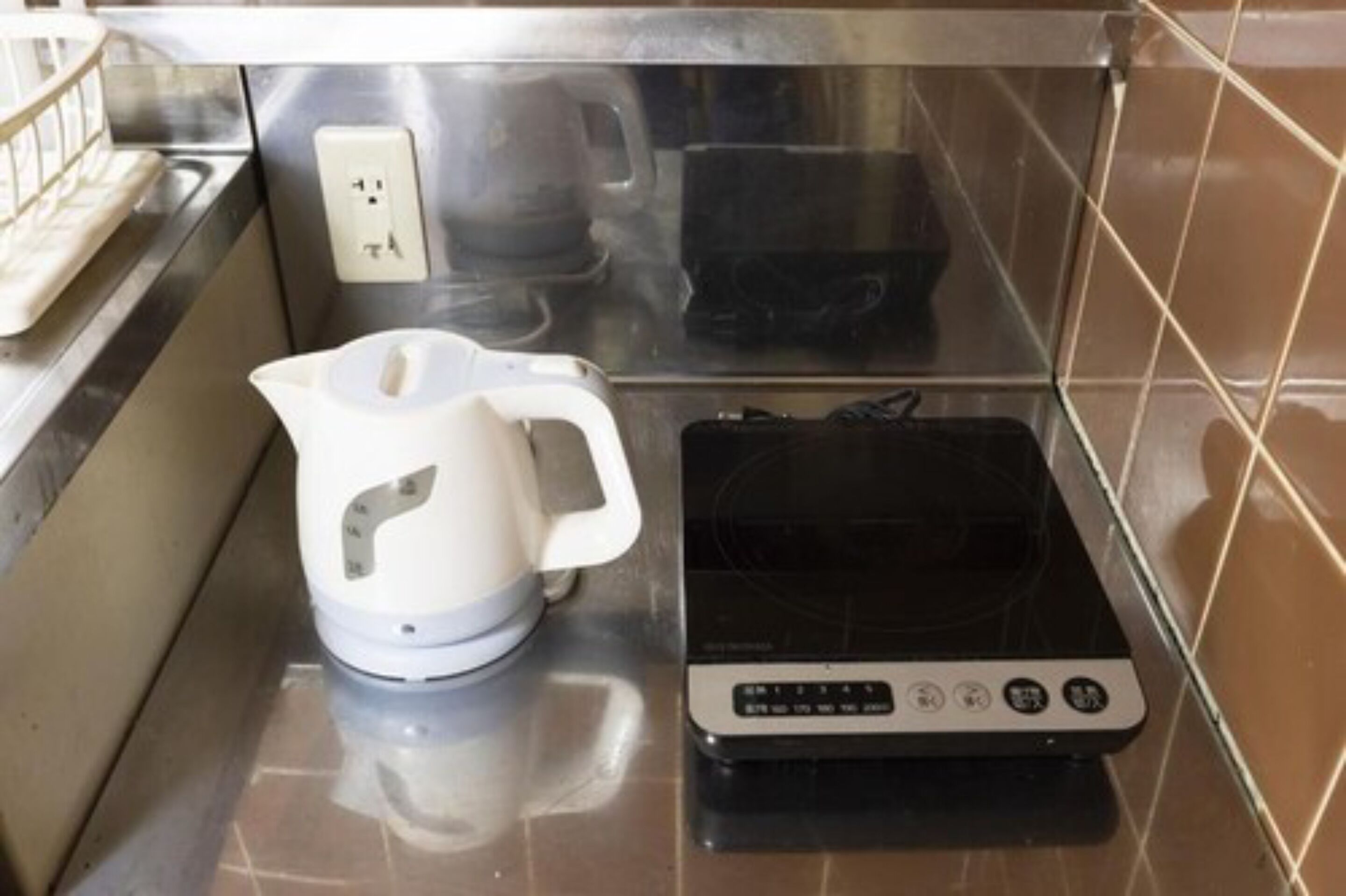 Cozinha com chaleira, fogão por indução preto e tomada.