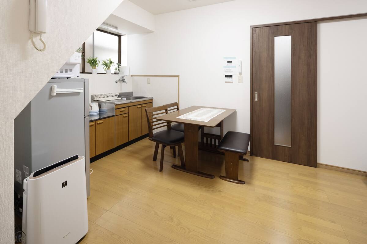 Cocina compacta con refrigerador, estufa y lavamanos. Hay una mesa de comedor con sillas y un gabinete de madera.