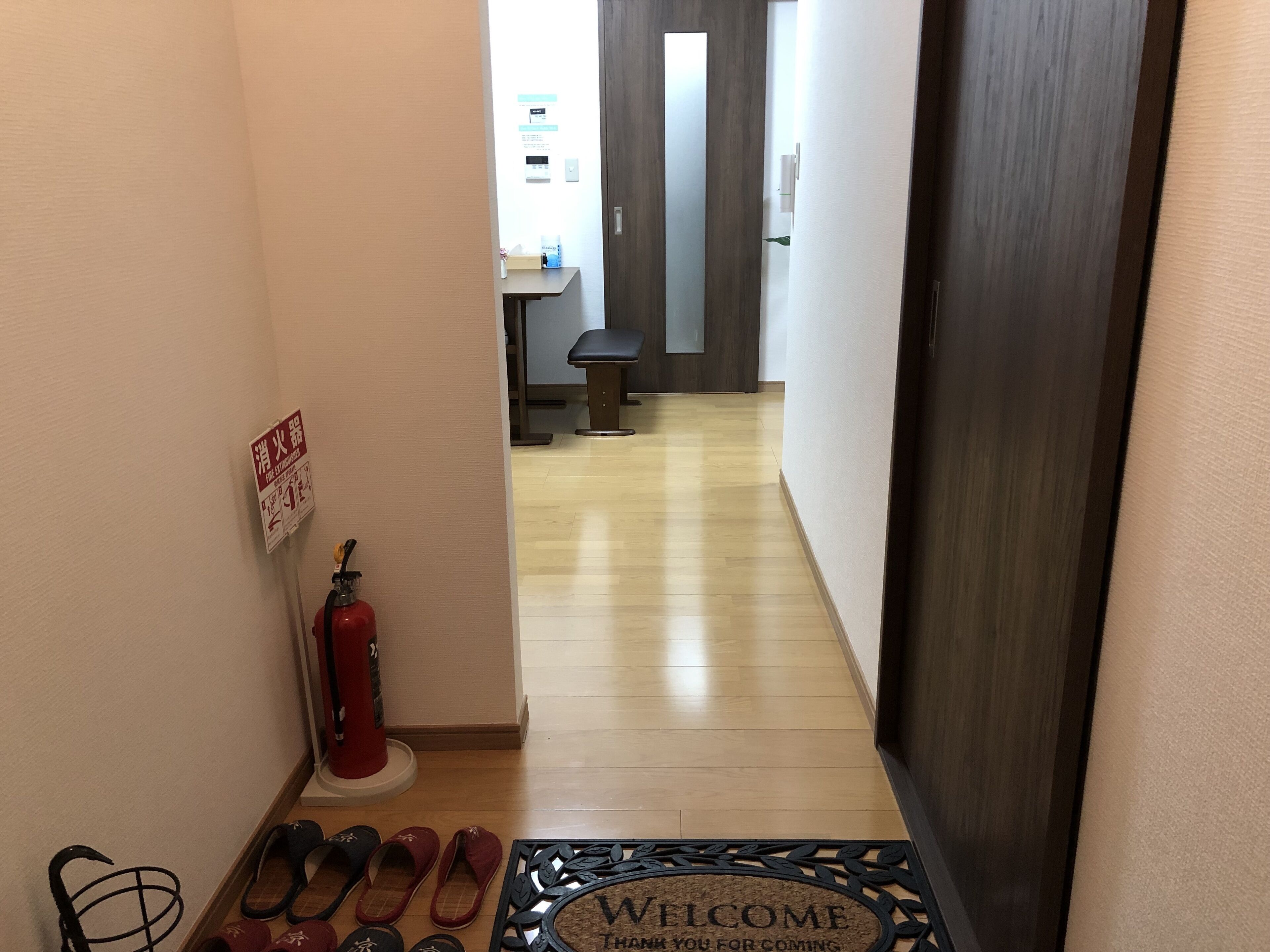A hallway with a fire extinguisher, a welcome mat, and a bench.