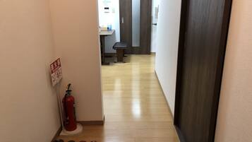 A hallway with a fire extinguisher, a welcome mat, and a bench.