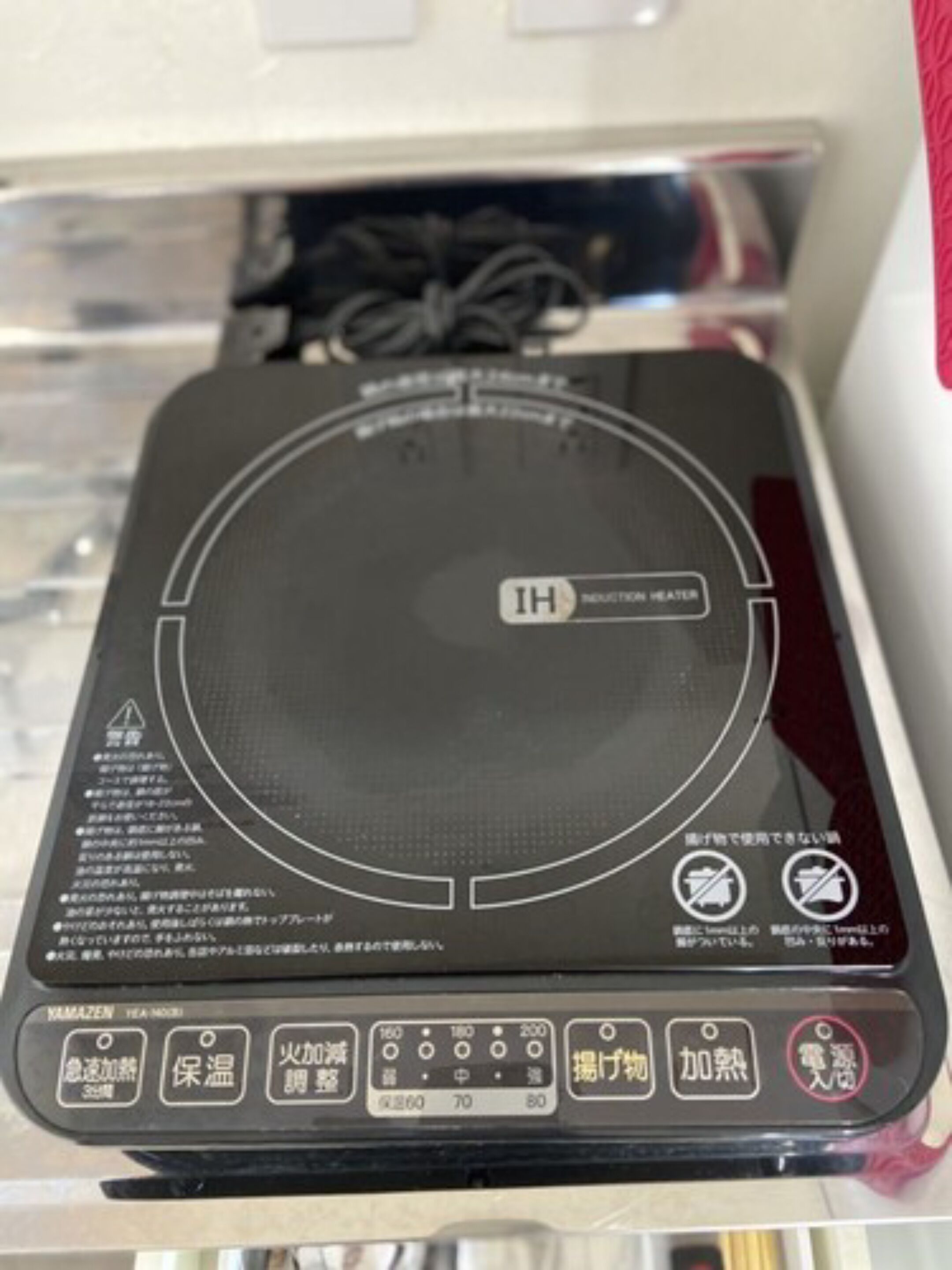 A black induction heater with Japanese labels and buttons for various functions.