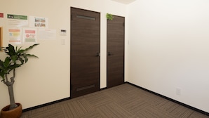 Un pasillo con dos puertas de madera oscura, una planta en maceta y carteles informativos en la pared.