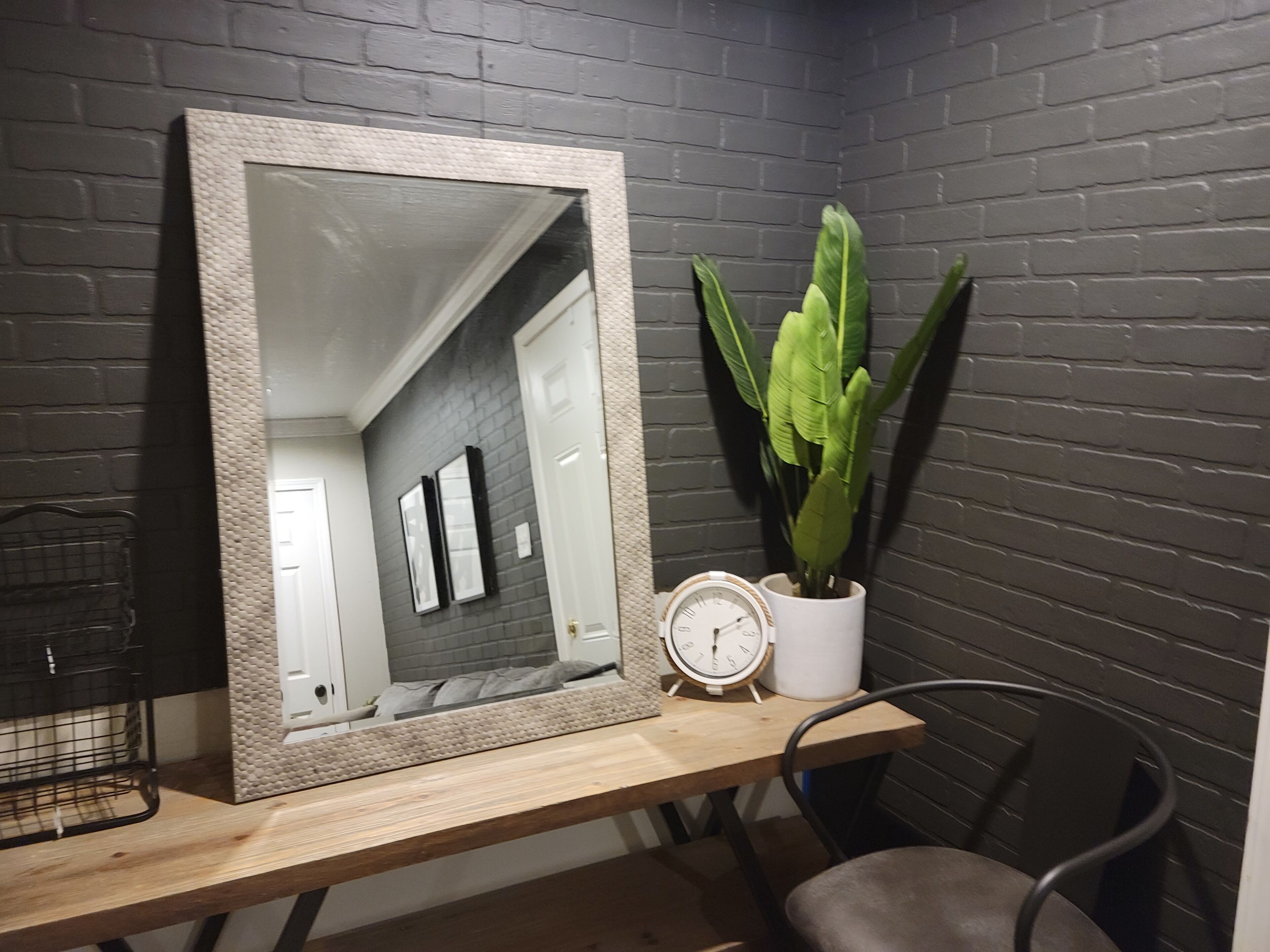 A mirror with a textured frame on a wooden desk, a potted plant, a clock, and a chair.