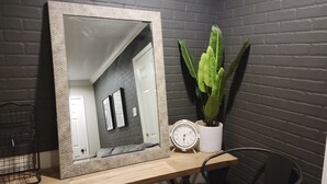 Un espejo con un marco texturizado sobre un escritorio de madera, una planta en maceta, un reloj y una silla.