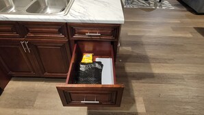 Una cocina con un lavamanos doble, armarios de madera y un cajón con una bolsa de papas.