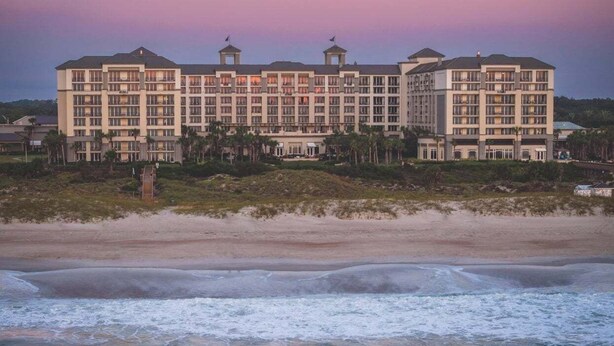 Ein mehrstöckiges Hotel mit symmetrischer Fassade, mehreren Balkonen und einer Strandlage.