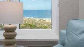 Ein Zimmer mit Blick auf das Meer durch ein Fenster, eine Lampe und ein blauer Sessel.