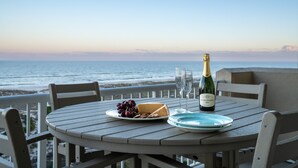 Ein runder Tisch mit einer Champagnerflasche, einem Käse- und Weinteller und einem Glas auf einem Balkon mit Meerblick.