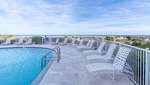 Ein Poolbereich mit weißen Metallstühlen und Blick aufs Meer.