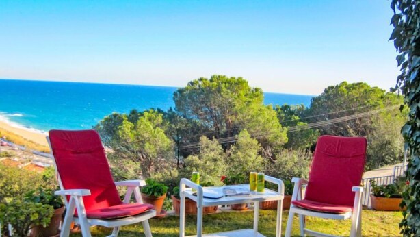Dos sillones rojos con una mesa blanca y plantas en macetas, con vista a una playa y al océano.