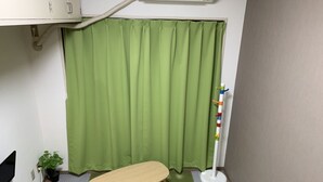 A room with a green curtain, a small wooden table, a colorful standing lamp, and a potted plant. - Guest House Zen Hakata (Fukuoka)