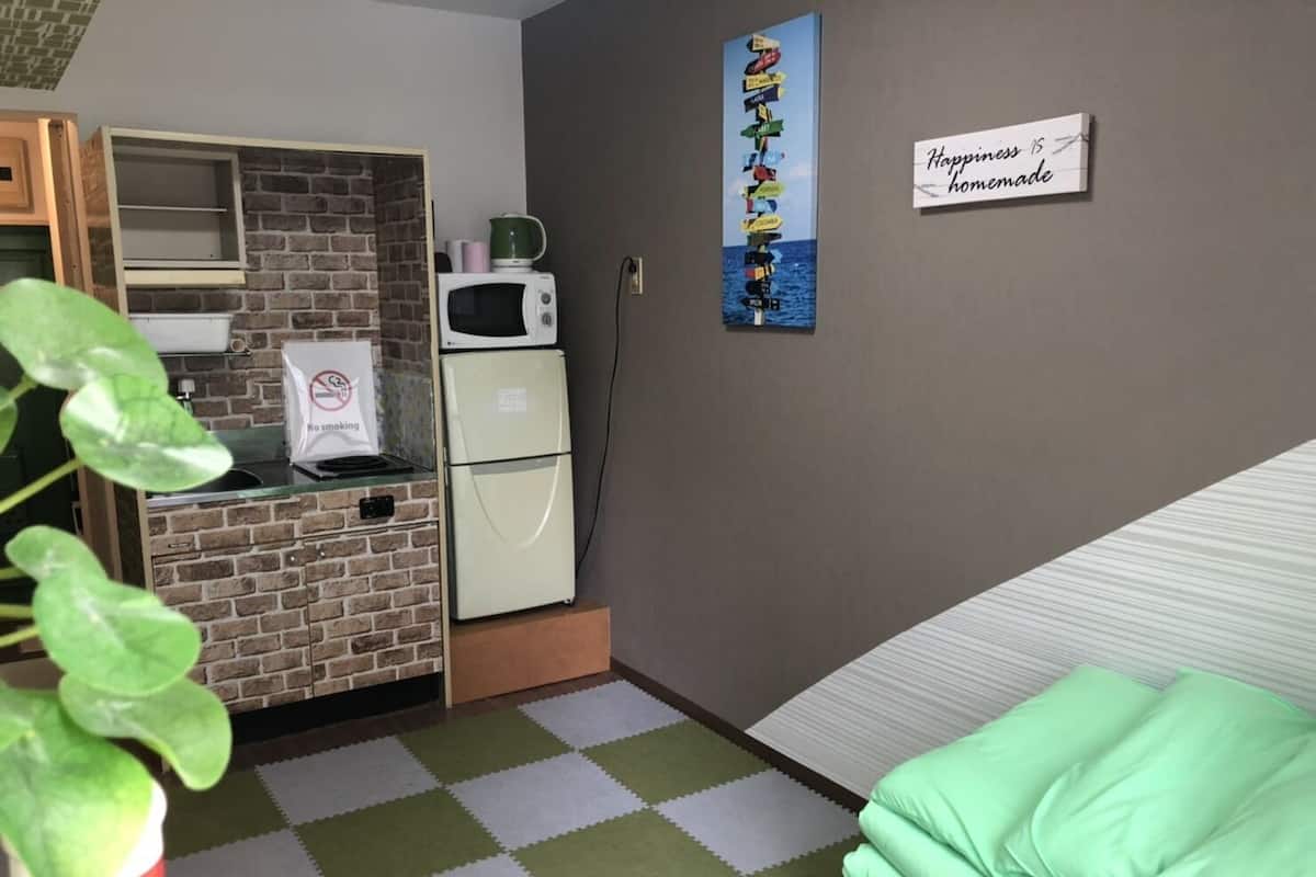 A compact room with a kitchenette, a bed, and a wall-mounted sign.