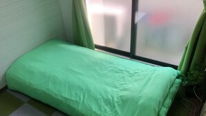 A small, single-bed room with a green bedspread, a window with green curtains, and a potted plant. - Guest House Zen Hakata (Fukuoka)