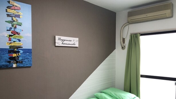 A room with a wall-mounted signpost with various country names and distances, a sign saying "Happiness is homemade," a window with a view of the sea, and a stack of green pillows. - Guest House Zen Hakata (Fukuoka)