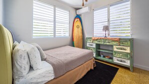 A bedroom with a bed, a dresser, a surfboard, and a window with blinds. - The Babanees - Bummer Hill Boho Chic Surf Shack  (Rincon)