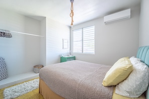 A bedroom with a bed, a window, a bedside table, and a hanging light fixture.