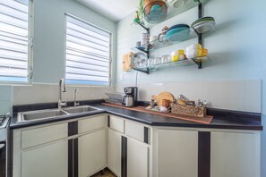 A kitchen with a black countertop, white cabinets, and a window with blinds.